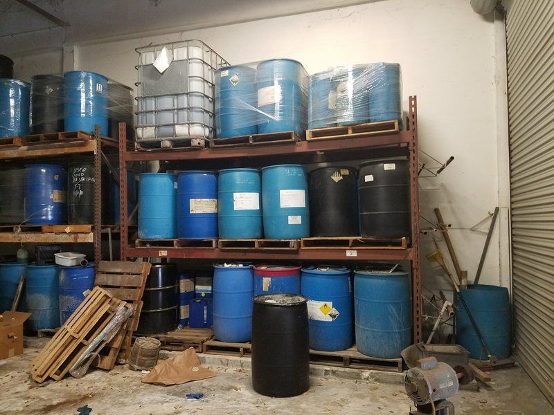 Drums and a tote stacked on metal racks