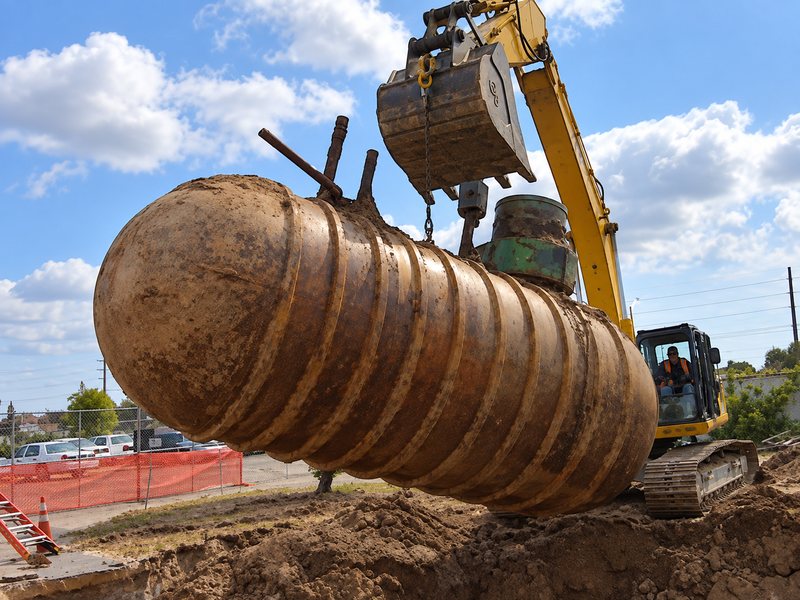 Excavator lifting a rusted underground tank